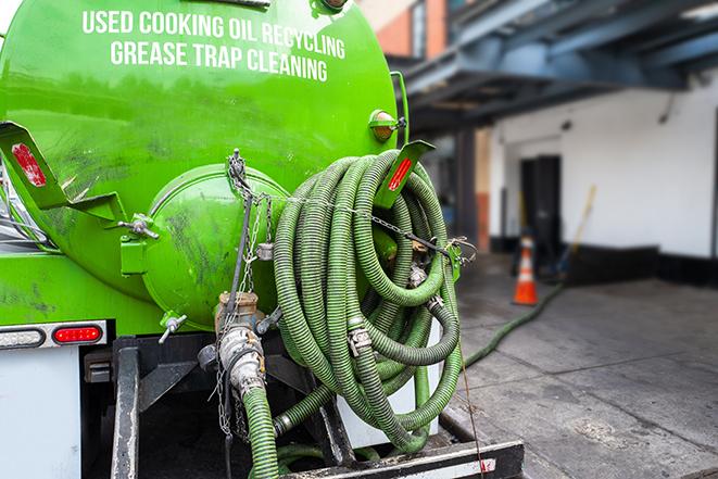 a professional plumber using a pump to empty a grease trap in Batavia